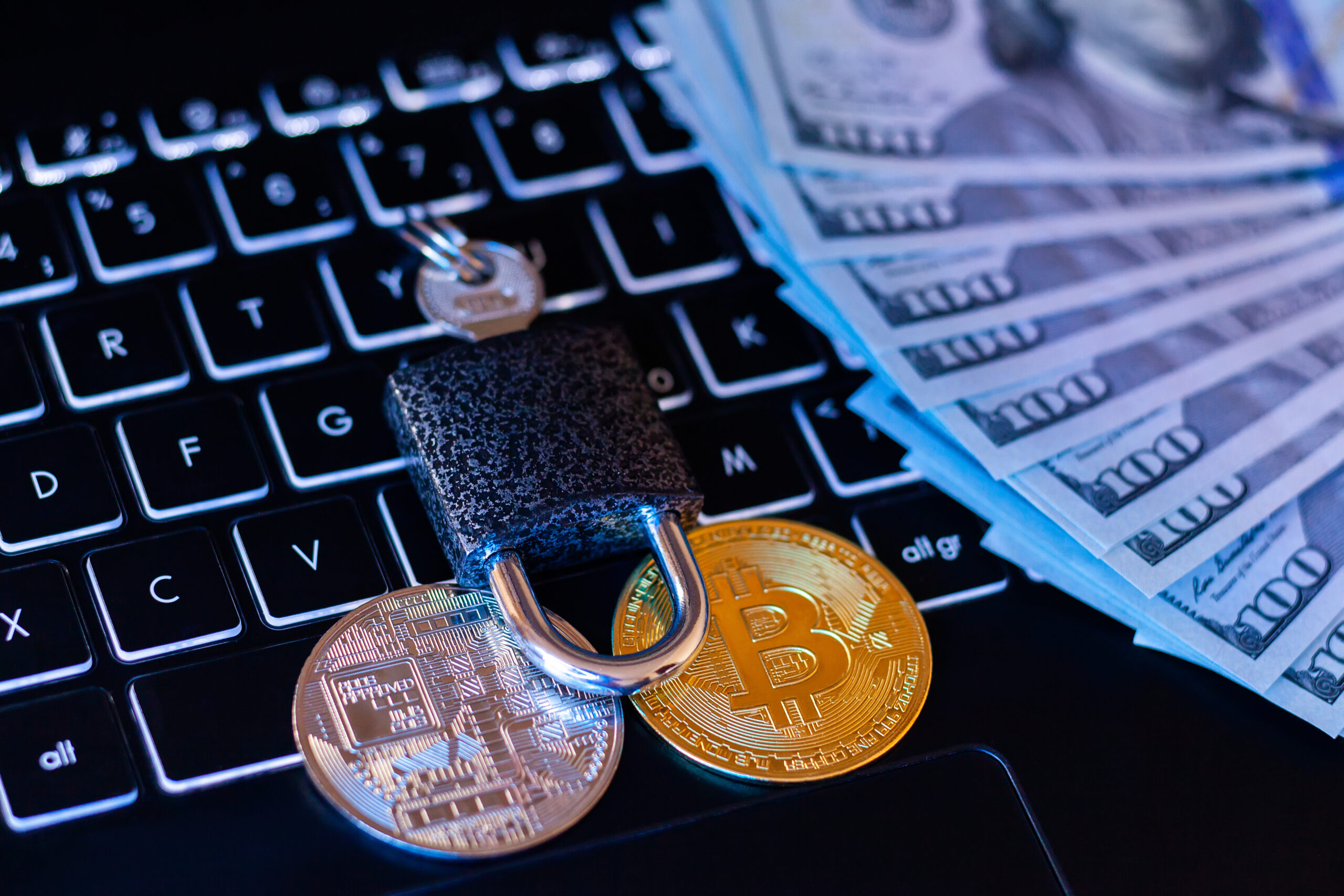 Prohibition of turnover and mining of cryptocurrencies. Bitcoin under lock and key on a laptop keyboard and hundred dollar bills in neon light.